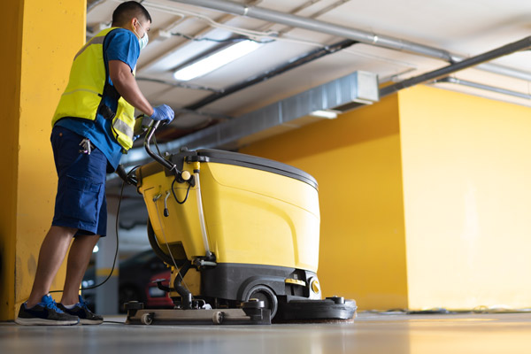 man walks behind floor scrubber in industrial setting