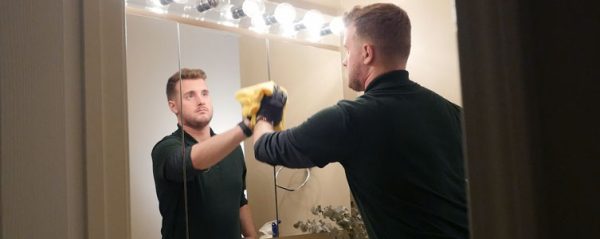 A man cleans a bathroom mirror with a cloth